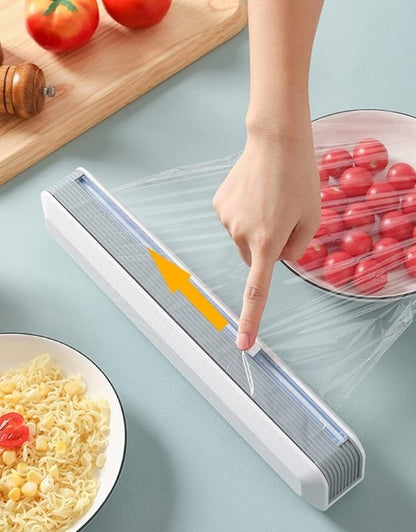 Person using a transparent rolling cling film dispenser on a kitchen counter.