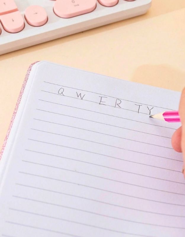 Notebook with 'QWERTY' letters written on it, held by a hand with a pink pencil.