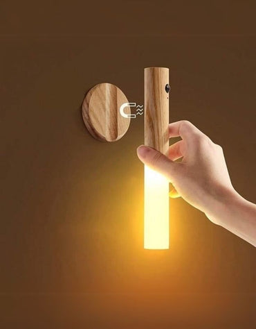 Hand removing portable LED lamp from magnetic wooden mount.