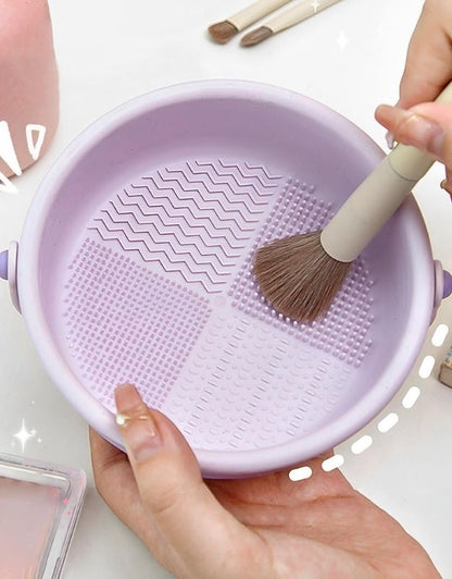 Hand cleaning makeup brush inside purple silicone cleaning bowl with scrub textures.