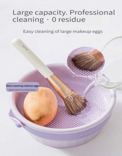 Makeup brush and sponge being washed in purple cleaning bucket with textured surface.