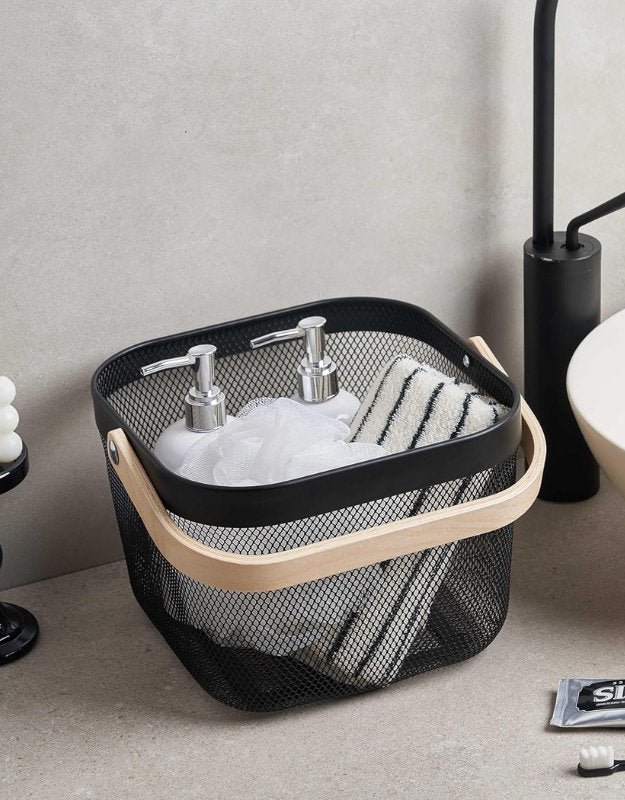 Black mesh storage basket with wooden handle holding bathroom toiletries and towels.