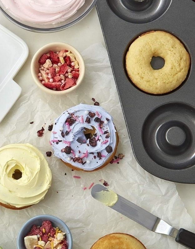 Donut-shaped baking pan with donuts and toppings on a light surface. Mini donut baking tray with freshly baked donuts, decorated with colorful icing and toppings.