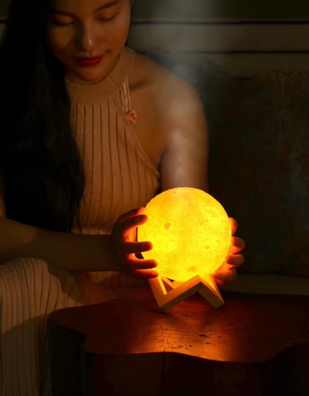 Woman holding glowing moon lamp humidifier with soft warm light in dark cozy room.
