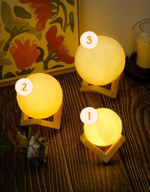 Three moon lamp humidifiers in small, medium, and large sizes glowing on wooden stands.