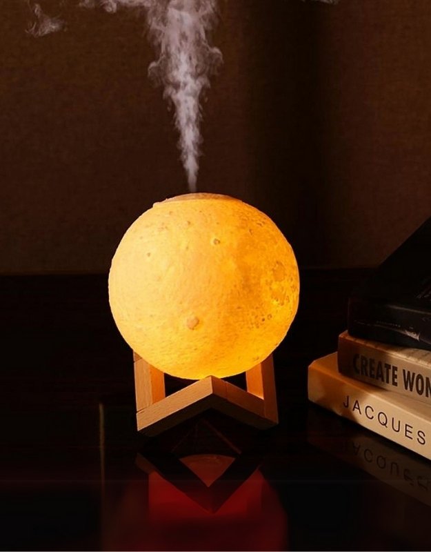 An essential oil diffuser designed to resemble a moon, emitting mist, placed on a wooden stand.
