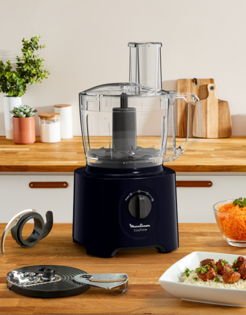 Moulinex Easy Force food processor displayed on kitchen counter with grating and slicing accessories beside prepared meals.