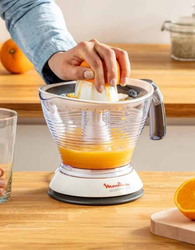 Person manually pressing orange on Moulinex Vita Press Juicer 1 L filled with fresh juice on kitchen counter
