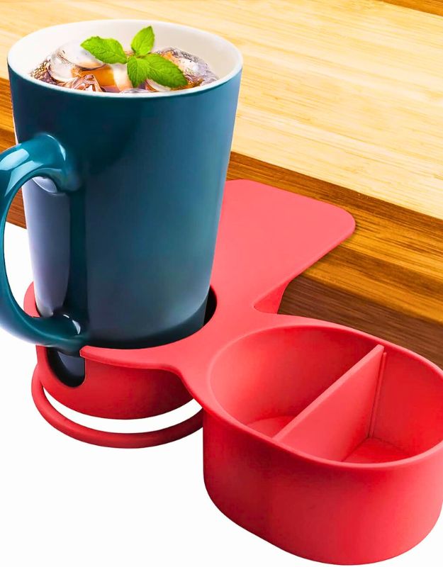 Side view of red mug holder clip attached to a wooden table, holding a blue mug and featuring a storage tray