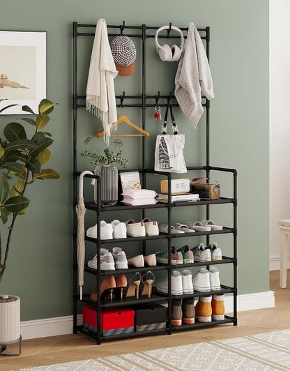 Multi-layer black metal shoe rack with coat hooks, jackets, hats, and shoes against green wall.