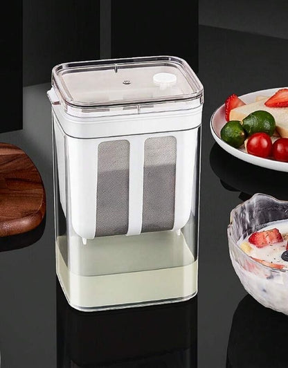 A multifunctional Greek yogurt and curd maker with a transparent lid and fine mesh strainer, displayed on a kitchen counter.