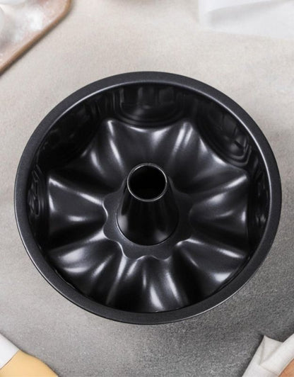 Black Bundt cake pan on a gray surface.  Top view of black nonstick bundt cake pan with central tube.
