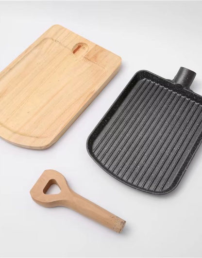 Wooden cutting board, black grill pan, and wooden bottle opener on a light background. Disassembled nonstick grill pan with detachable wooden handle and serving tray.