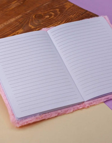 Open plush-covered notebook with ruled pages on a wooden and pastel background.