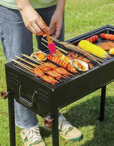 Charcoal barbecue grill with skewers and corn cooking outdoors.