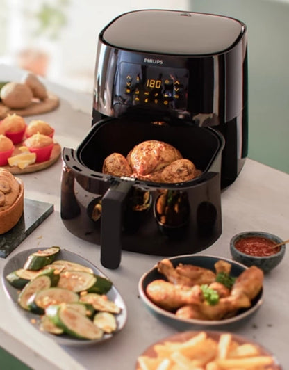 Philips airfryer with roasted potatoes and side dishes on table.