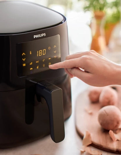 Hand using Philips airfryer touchscreen with cooking presets.