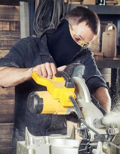 Man wearing black balaclava mask and safety glasses while using a power saw.