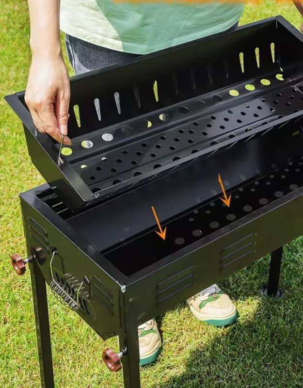 Removable charcoal tray inside black metal BBQ grill.
