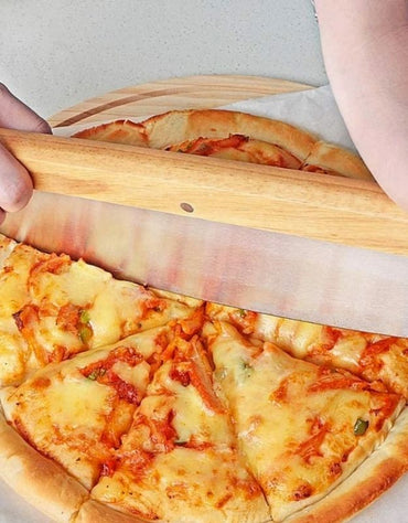 Person using a wooden pizza cutter to slice a pizza on a white surface. Close-up of rocker pizza cutter slicing a cheese pizza with vegetables.