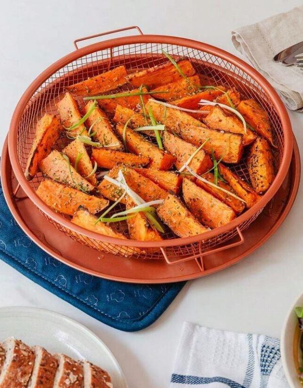 Seasoned sweet potato wedges in a round air fryer basket on a kitchen table