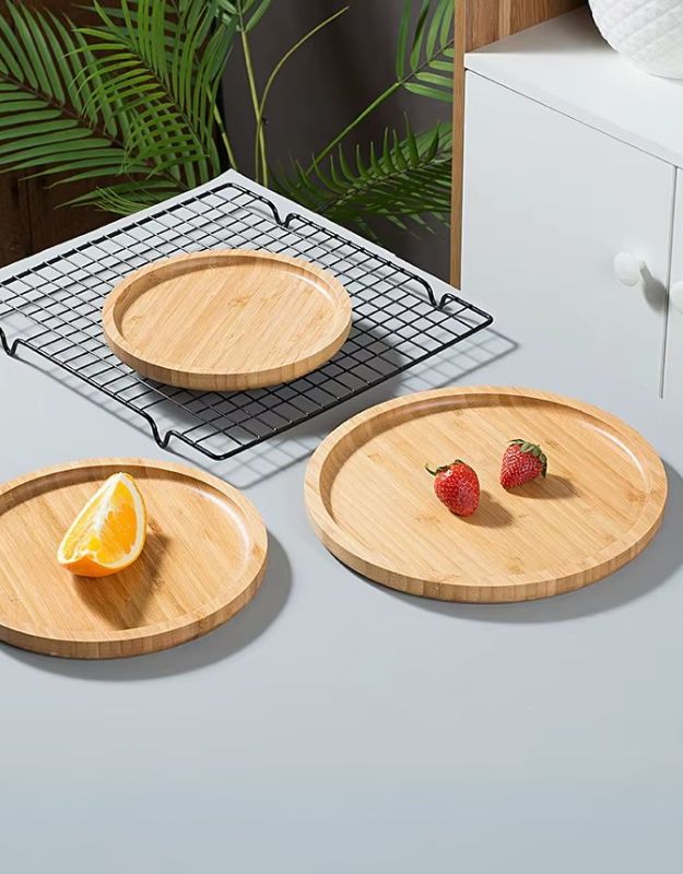 Three bamboo wood serving trays with a rounded shape and raised edges, displayed on a white surface, one with a lemon slice, one with strawberries, and one empty.