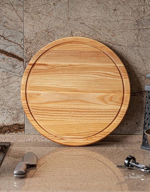 Round wooden cutting board on a marble surface. Empty round wooden chopping board displayed on kitchen counter.
