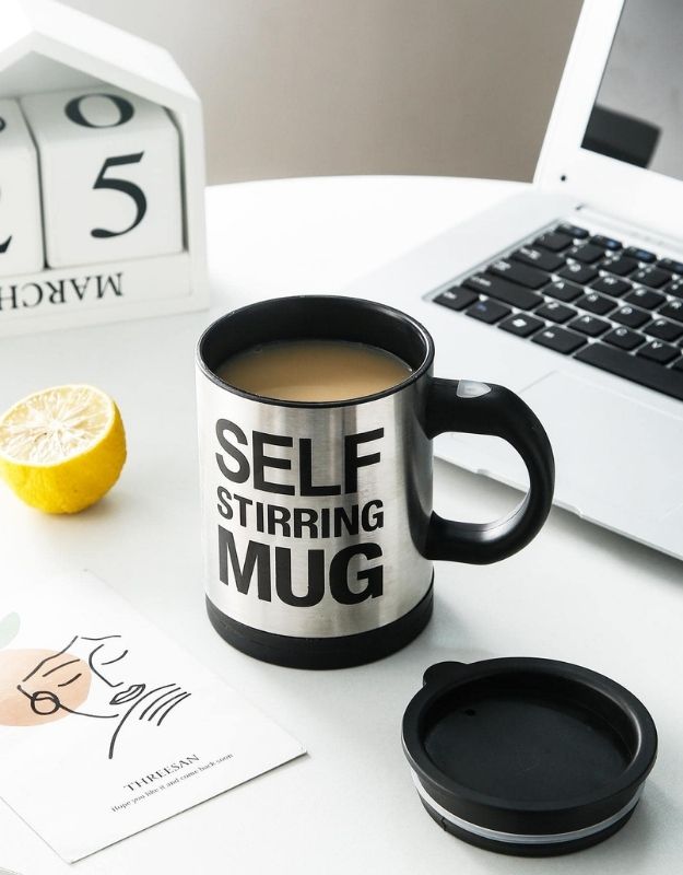 Self-stirring mug filled with coffee on desk beside laptop and lemon slice.