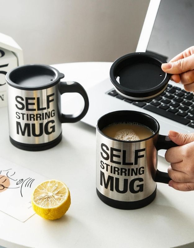 Self-stirring mug with lid being placed on, next to another mug and a lemon slice.