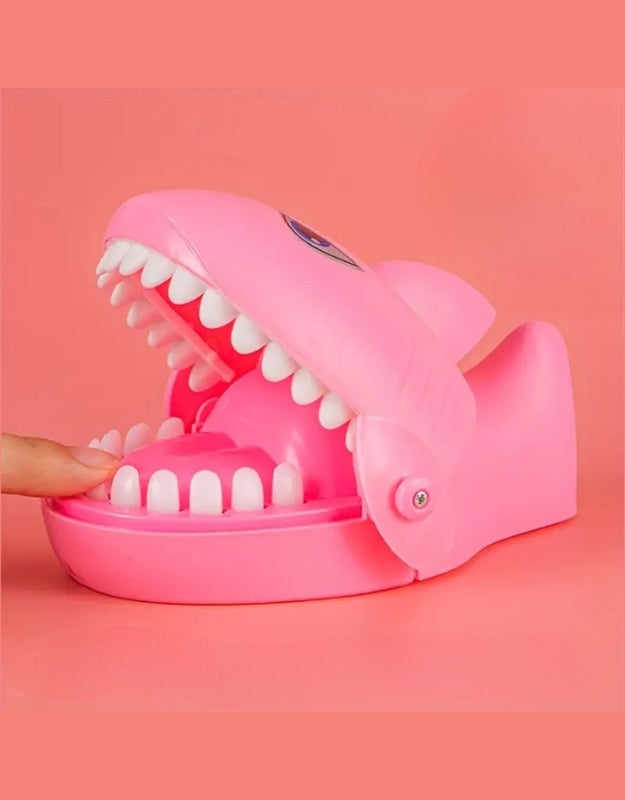 A side view of the pink "Shark Dentist" game with a hand about to press a tooth inside its open mouth