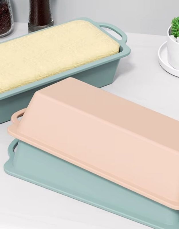 Two silicone bread loaf pans, one green and one beige, on a white surface. Baked loaf inside silicone pan with nonstick easy release design.