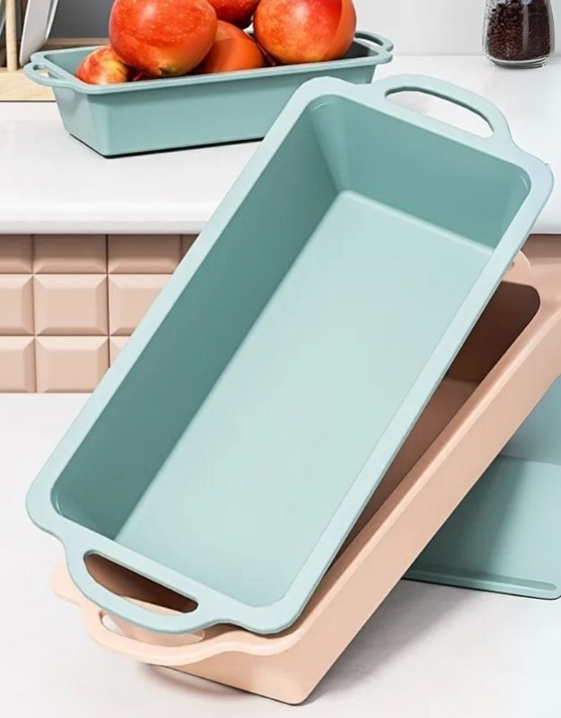 Light blue loaf pan on a kitchen counter with apples in the background. Stacked blue and pink silicone loaf pans on a kitchen counter.