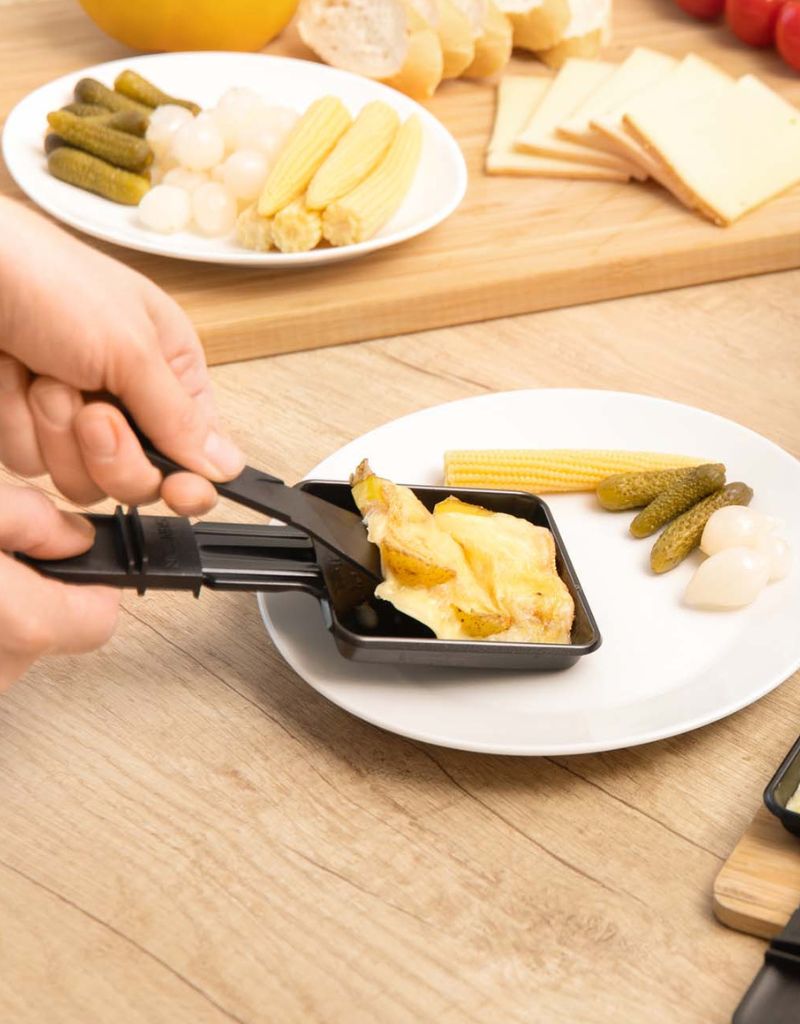 Person serving melted cheese and grilled vegetables from Silver Crest raclette grill onto a plate