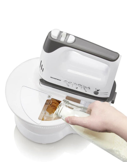 Silver Crest 300W stand mixer with user pouring milk into mixing bowl through transparent lid