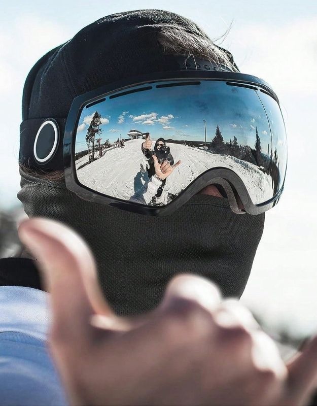 Person wearing ski mask balaclava with goggles while snowboarding.