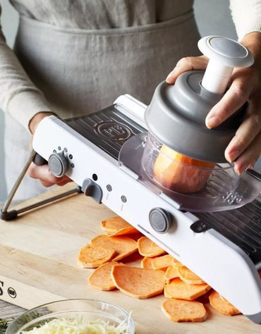 Person using a kitchen slicer to cut sweet potatoes on a wooden board. Mandoline slicer with safety hand guard cutting vegetables.