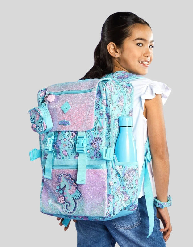 Smiggle foldover seahorse school backpack shown on a girl, featuring side bottle holder and glitter seahorse design