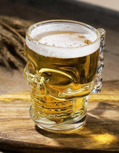 Skull-shaped glass mug filled with beer on a wooden surface.