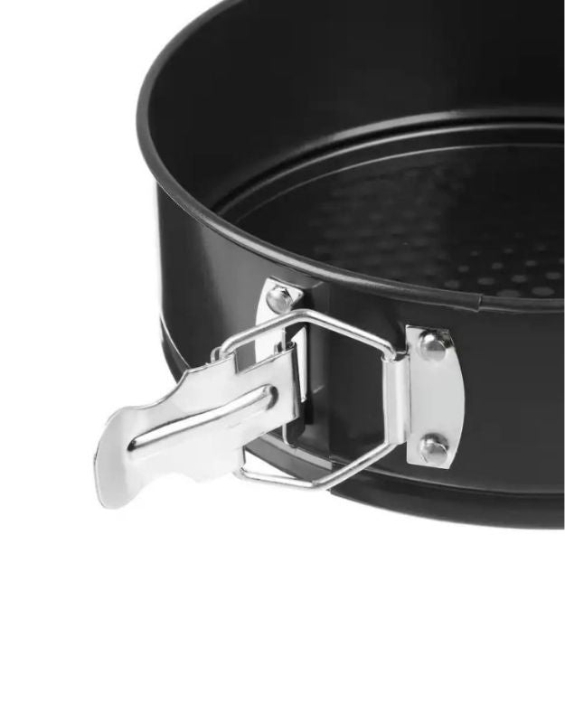 Black springform pan with a chrome clasp on a white background. Close-up of springform cake pan latch mechanism on nonstick bakeware.