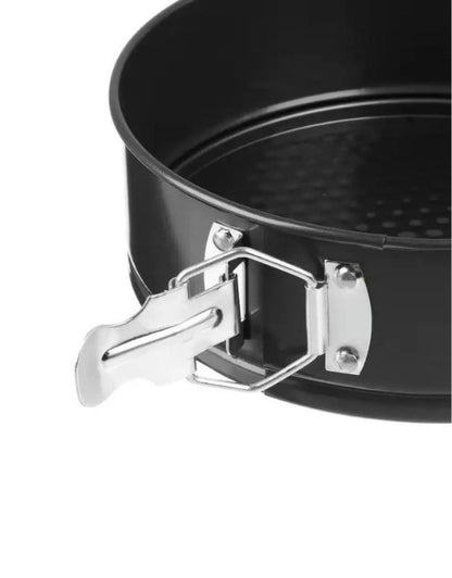 Black springform pan with a chrome clasp on a white background. Close-up of springform cake pan latch mechanism on nonstick bakeware.