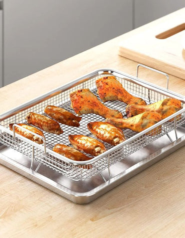 Crispy chicken wings and drumsticks cooking on stainless steel crisper basket over tray on kitchen counter