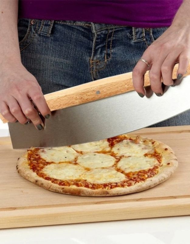 Person cutting a pizza with a wooden pizza cutter on a wooden board. Person cutting pizza with a stainless steel rocker style pizza cutter with wooden handle.