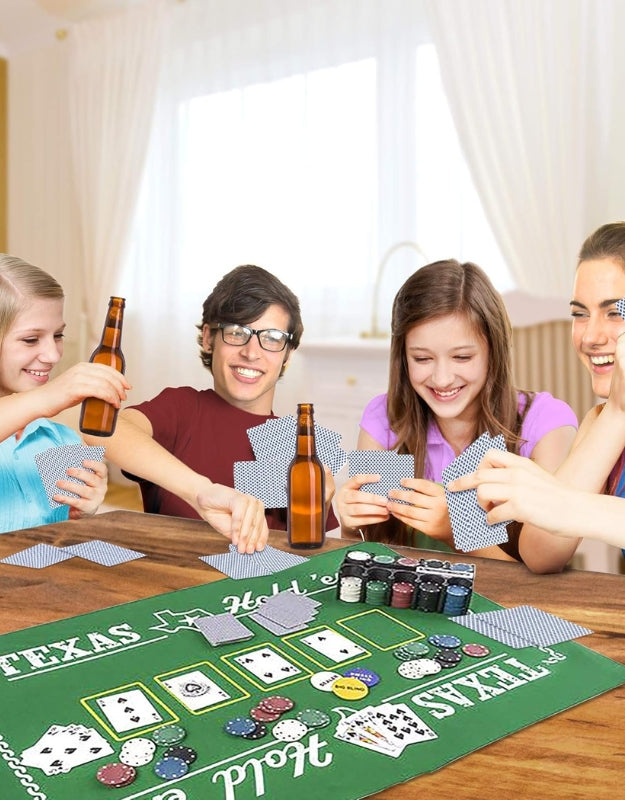  A group of teenagers or young adults laughing and playing a game of poker with the Texas Hold'em set on a wooden table
