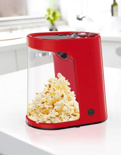 A red popcorn maker with a transparent container filled with popcorn, placed on a kitchen countertop.