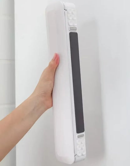 Hand holding a white electronic device against a white background. Hand holding wall-mounted plastic wrap dispenser with non-slip backing.