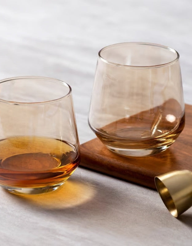 Two glasses of amber liquid on a wooden coaster with a white background. Two whiskey glasses with golden drink on wooden tray and marble surface.