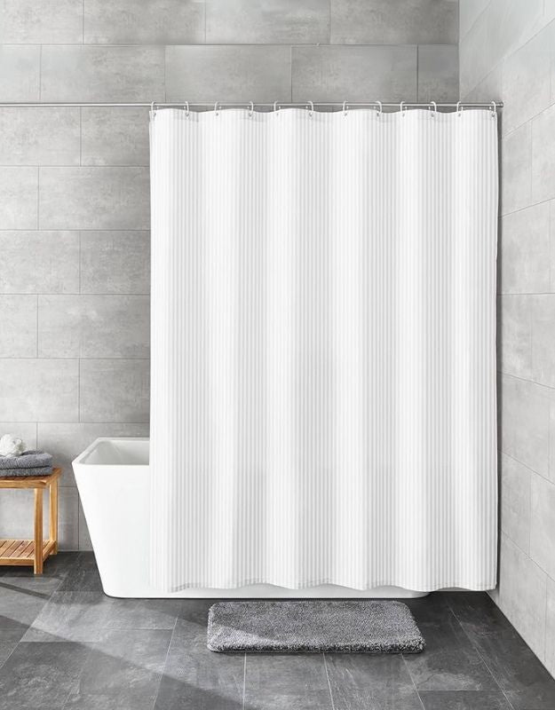 A white, rectangular shower curtain with metal grommets hanging in a bathroom setting. Full white striped shower curtain covering bathtub in modern bathroom.