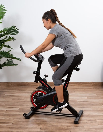 Woman using indoor silent exercise bike in a home gym setup with wooden flooring and plant decor.