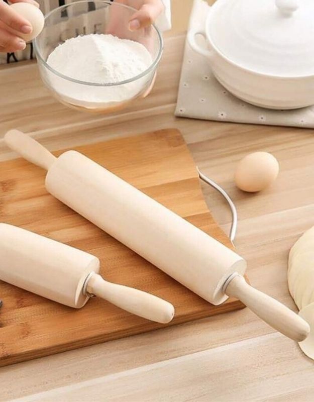 Two rolling pins on a wooden board with flour and eggs in the background. Wooden rolling pin on kitchen table with flour and eggs, perfect for baking and dough rolling.