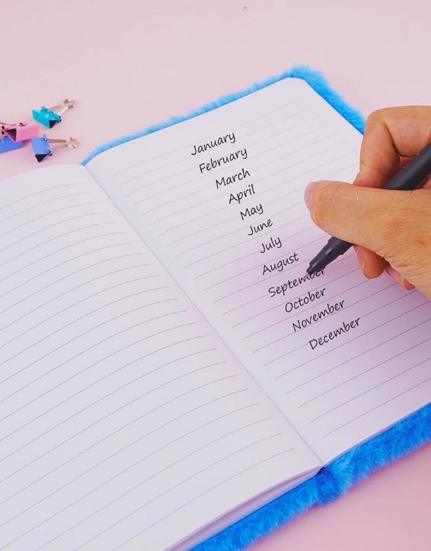 Hand writing months of the year in a notebook on a pink background
